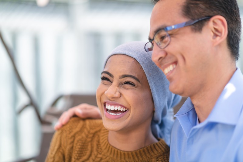 Woman with headscarf smiling. Mans arm around her shoulder