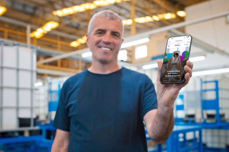 A man displays a smartphone featuring a Teladoc Nutrition and Fitness Consult app on its screen.