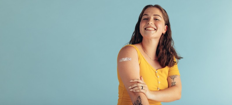 A woman displaying band-aid on her arm, a wearing yellow top..