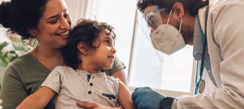 A doctor examines a child while a woman gently holds the child's hand for comfort during the check-up.