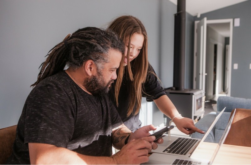 A father and daughter engaged in a discussion while submitting a claim on a laptop in a bright workspace.