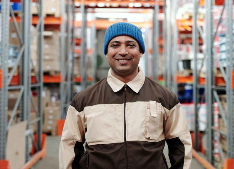 man, employee, posing for a phot in a warehouse, with his work clothes on.