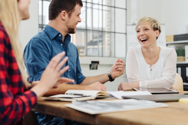 Three people at a table laughing and engaging in conversation, creating a lively and cheerful atmosphere.