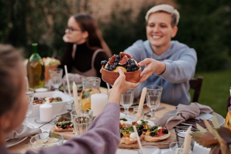 A diverse group of people gathered around a table, enjoying a meal together with various dishes and drinks.